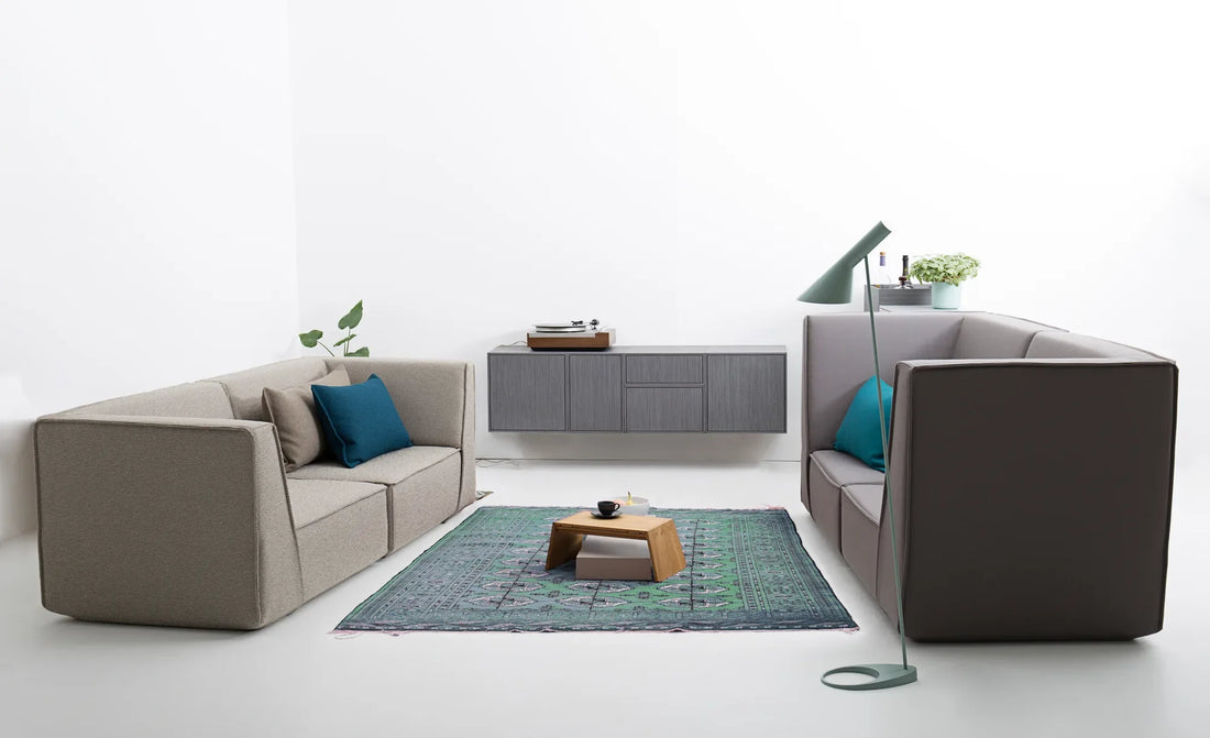 Wohnzimmer mit großem grau-beigem Sofa, Holzsideboard, grünem Teppich und Couchtisch.