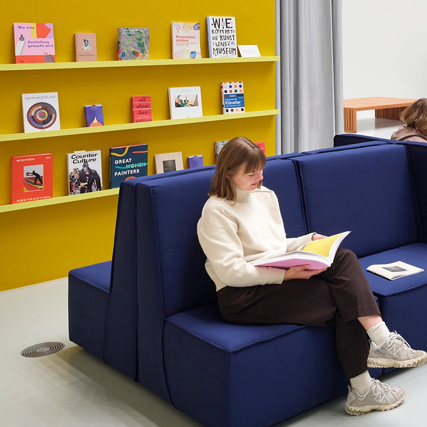 Modulare Sofaelemente in einem modernen Bildungs- und Ausstellungsraum mit gelber Wand.