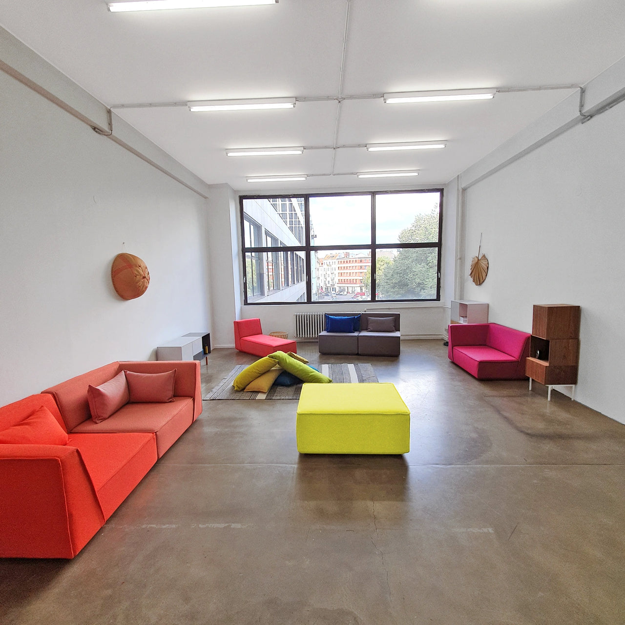 Spacious Showroom in Berlin with various Cubit sofa modules in bold colours in front of a window front with a city view, complemented by Sideboards and carpet on a concrete floor.