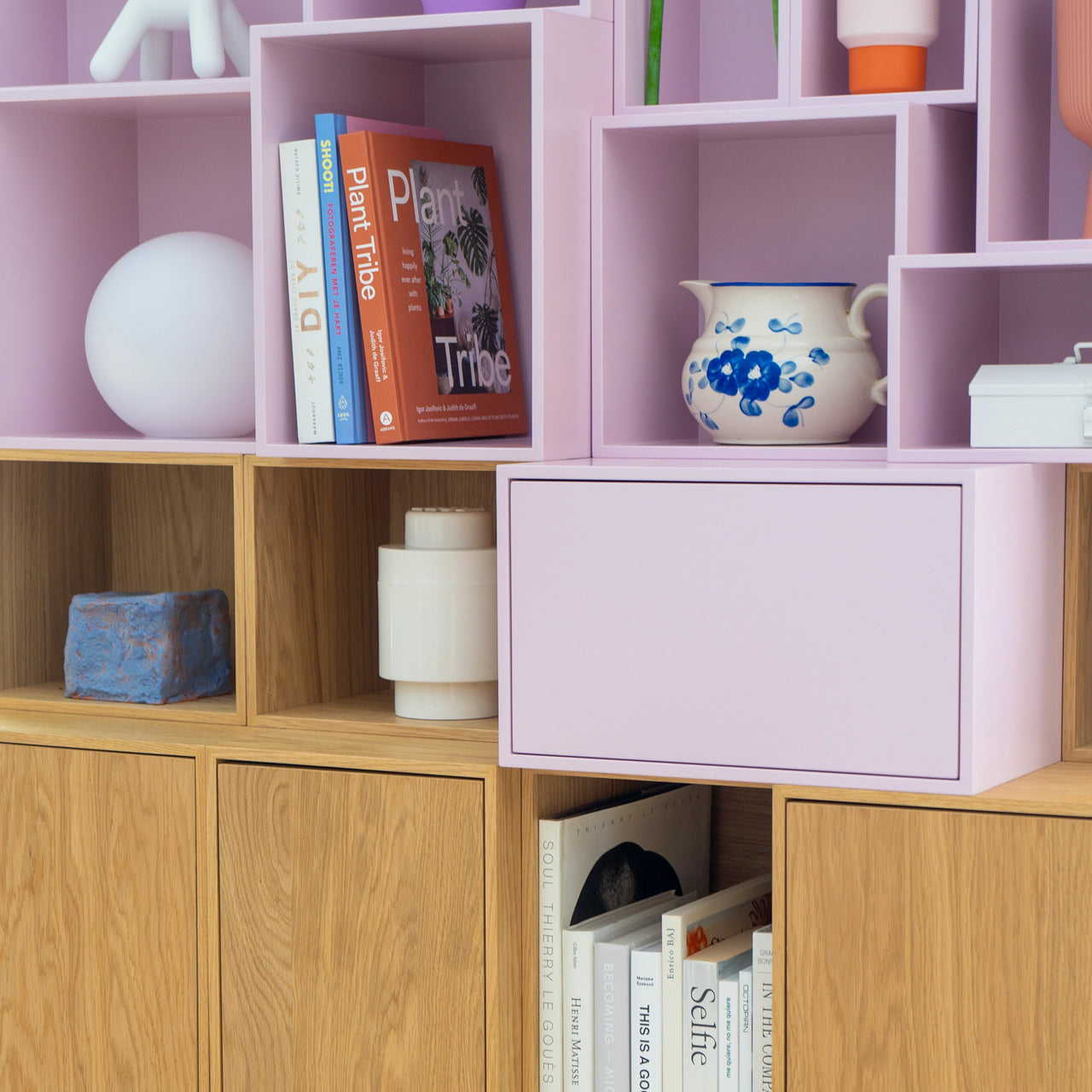 Detailansicht eines modularen Regals mit pastellrosa und Holzmodulen, bestückt mit Büchern und Dekorationsobjekten