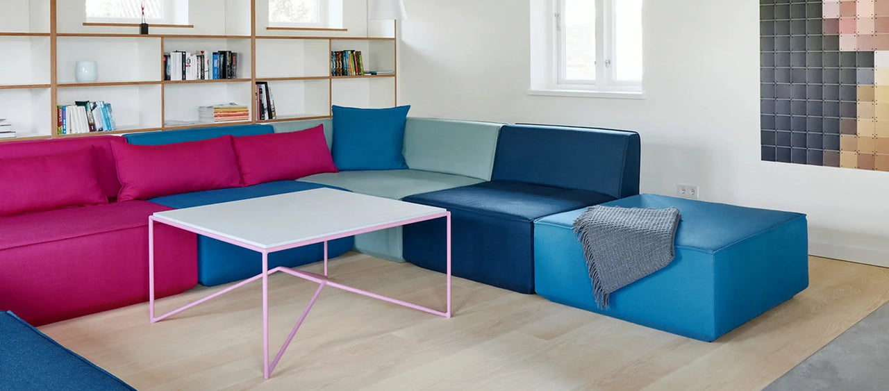 canapé modulable et bleu avec une étagère en bois et une table basse rose dans le salon d'un immeuble ancien.
