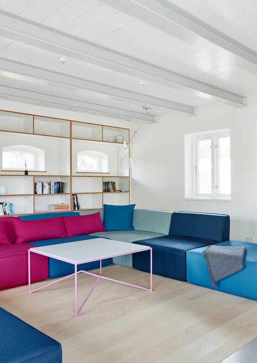 canapé modulable et bleu avec une étagère en bois blanc et une table basse rose dans un immeuble ancien.