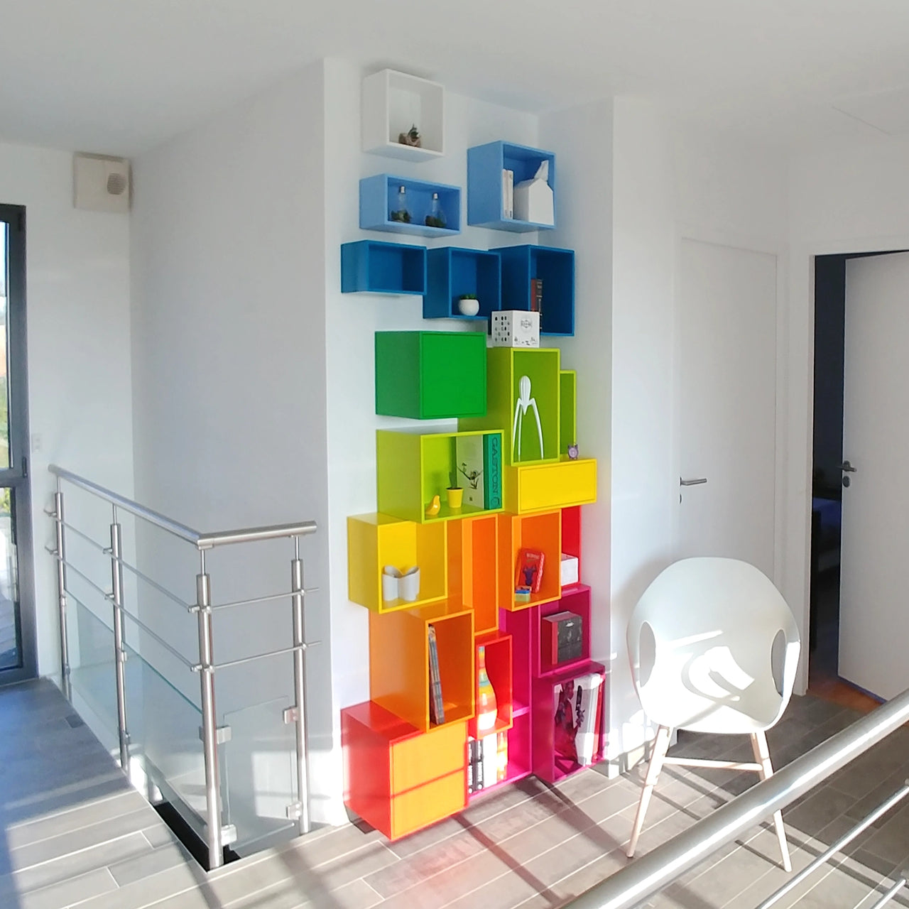 An open shelf made of different coloured cubes - from blue to pink - fits perfectly into a wall niche