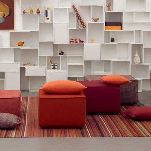Poufs in Rot und Orange auf gestreiftem Teppich, kombiniert mit moderner Regalwand.
