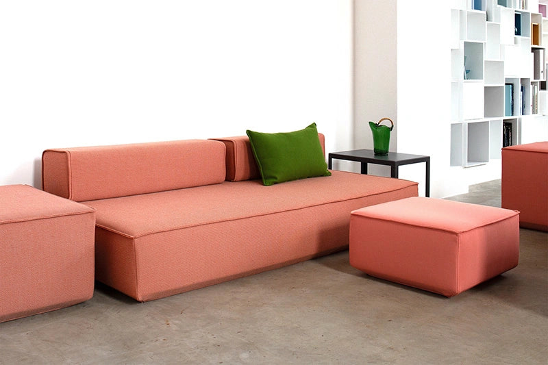 Ein korallenfarbenes modulares Schlafsofa mit passendem Hocker und einem grünen Kissen mit Modularen Rückenlehnen.