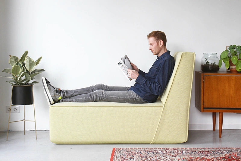 Ein Mann sitzt lesend auf einem Hellgelben Cubit Sofa-Modul in einem modern eingerichteten Wohnzimmer mit Retro-Sideboard und Zimmerpflanzen.