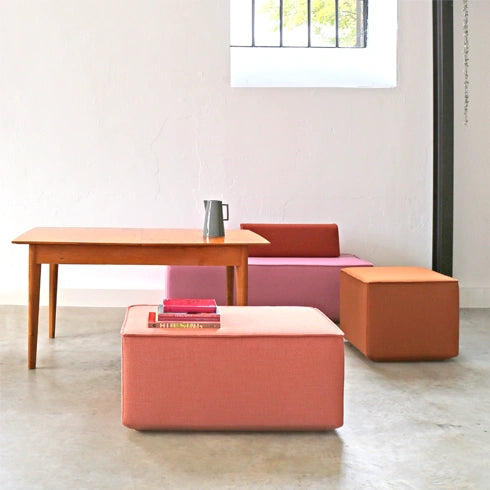 Modulare Sitzbänke in Rosa-, Orange- und Rottönen mit Holztisch und Fenster in modernem, hellen Raum mit Betonboden