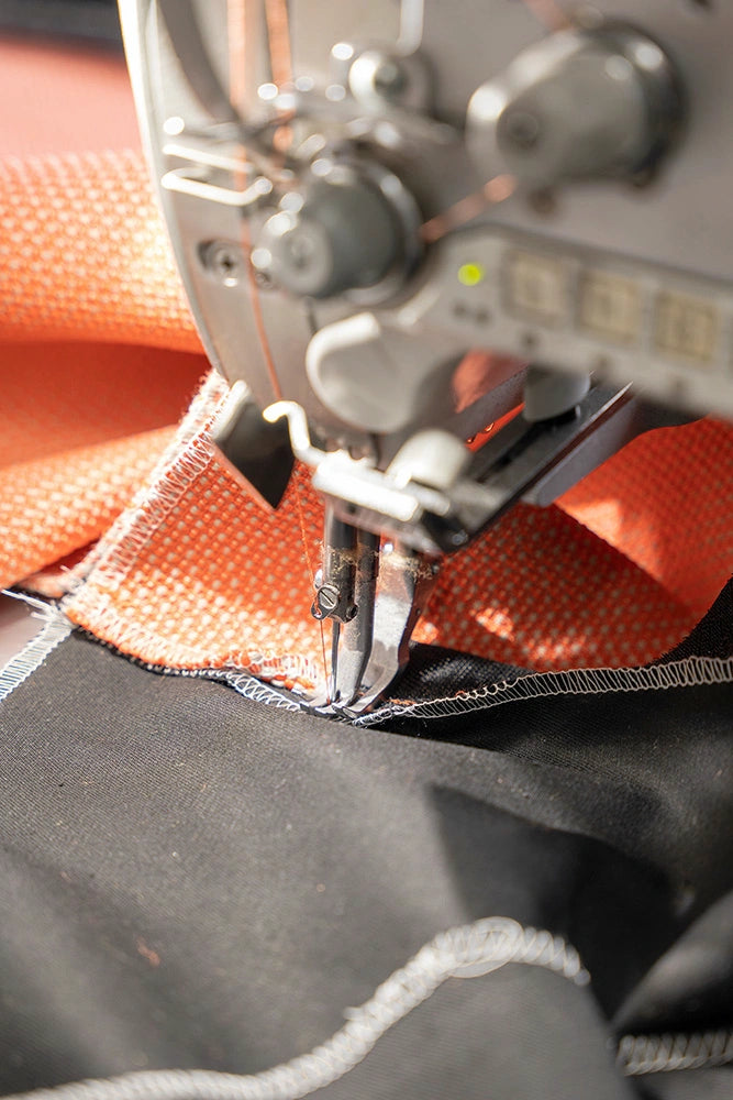 Detailaufnahme einer industriellen Nähmaschine, die einen robusten orangefarbenen Polsterstoff präzise verarbeitet.