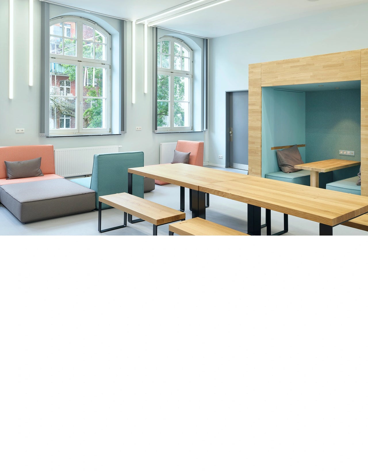 Moderne Sofalandschaft mit farbigen Modulen und integrierten Sitznischen in einem hellen Gemeinschaftsraum eines Gymnasiums